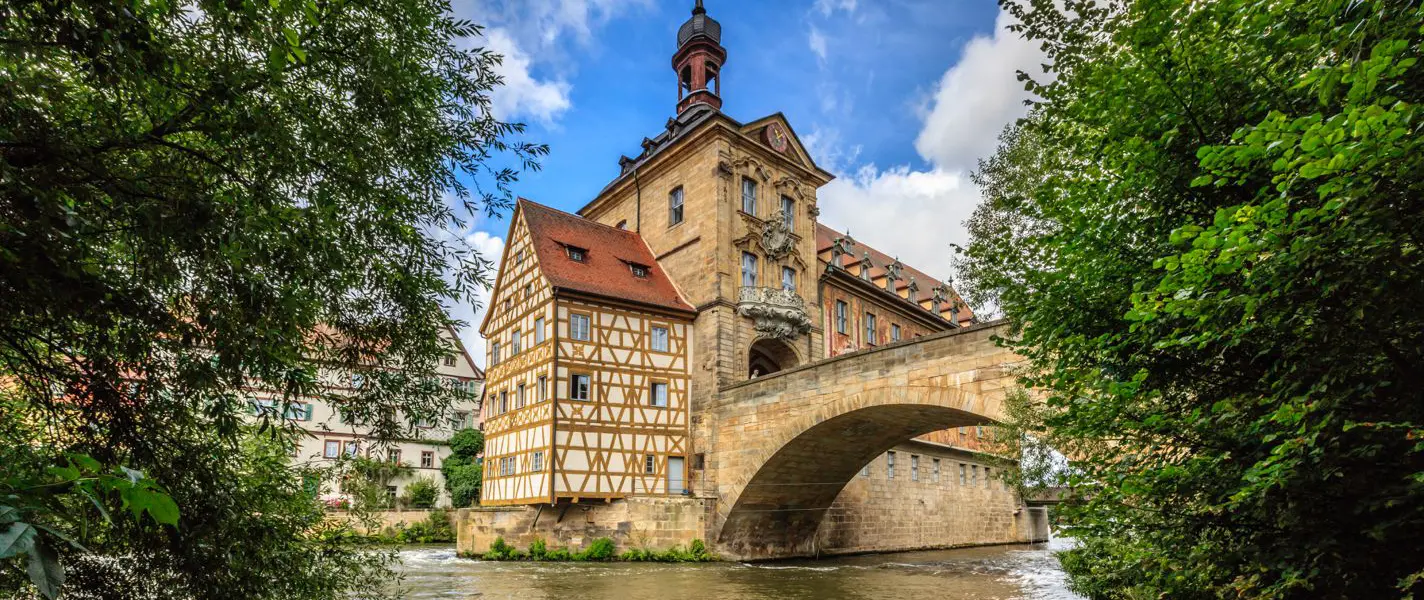 Historisches Fachwerkhaus mit steinbrücke über Fluss und grünen Bäumen unter blauem Himmel als Beispiel für gelungene Bildgestaltung