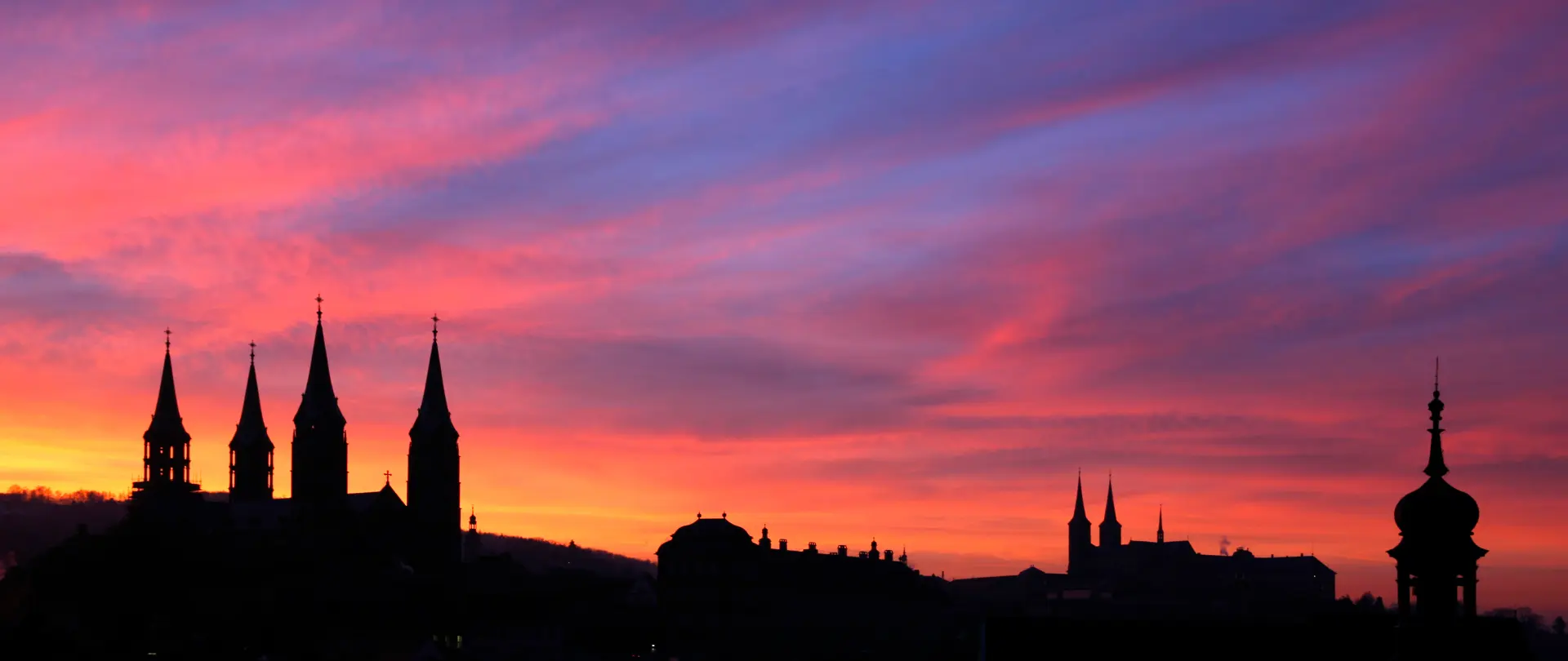 Sonnenuntergang mit farbigem Himmel über der Silhouette von Bamberger Kirchtürmen und historischen Gebäuden