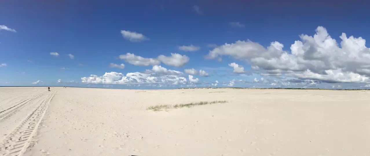 Weite Sandfläche am Strand von Amrum mit blauem Himmel und vereinzelten Wolken, ideal für kreative Naturfotografie