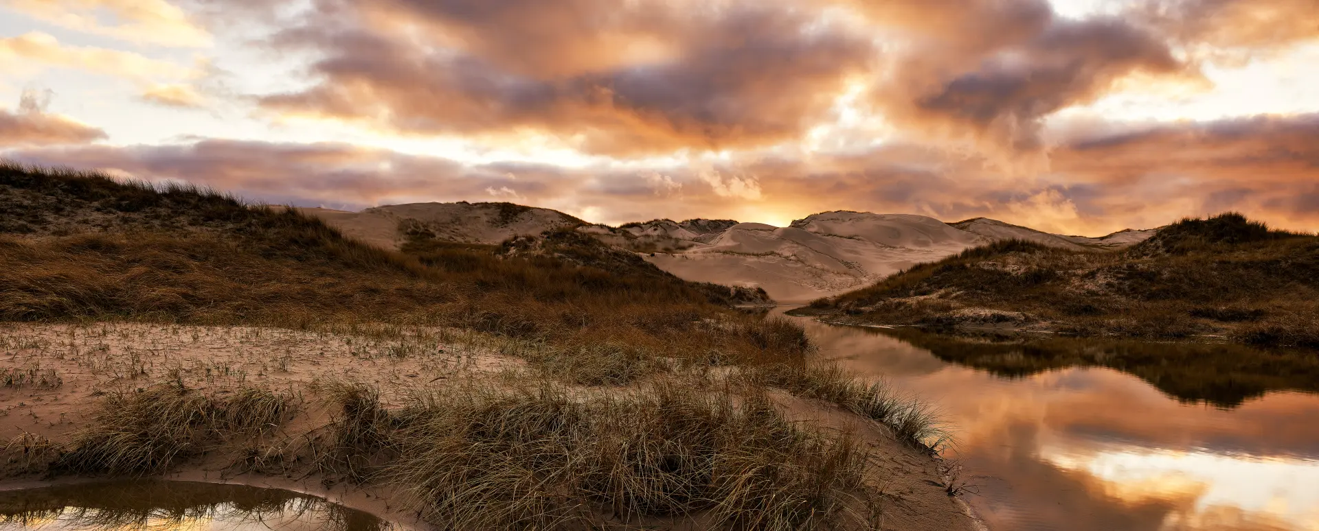 Sanddünen und Wasserpfützen bei Sonnenuntergang auf Amrum mit reflektierendem Himmel und herbstlicher Landschaft am Meer