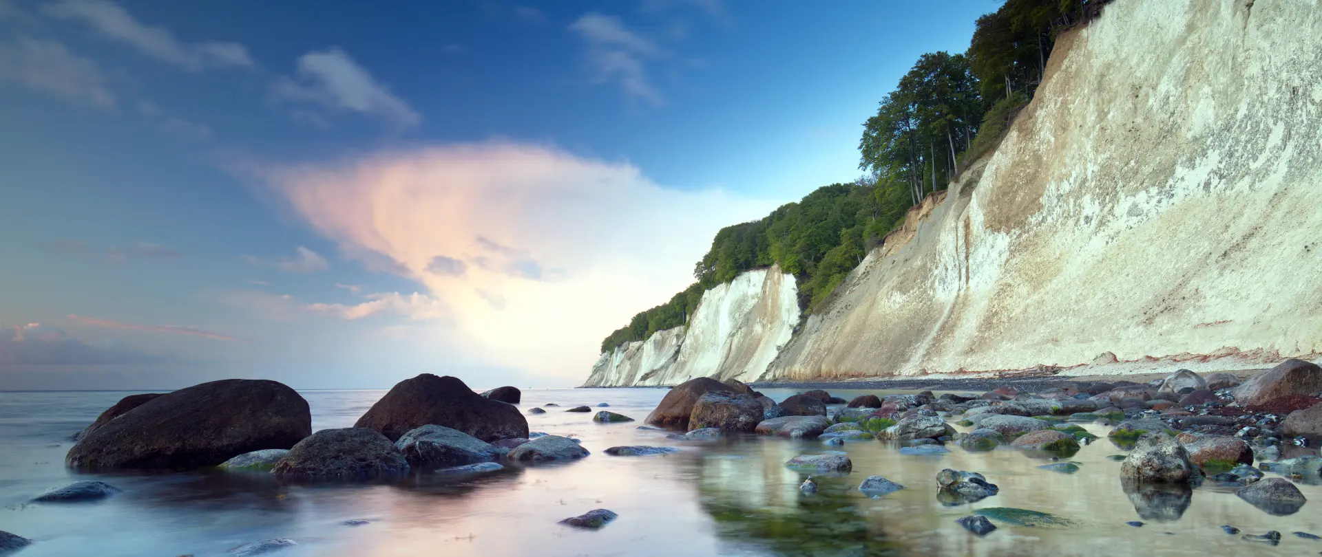 Kreidefelsen an der Herbstküste von Rügen mit Felsen im Wasser und bewaldeten Uferabschnitten unter blauem Himmel