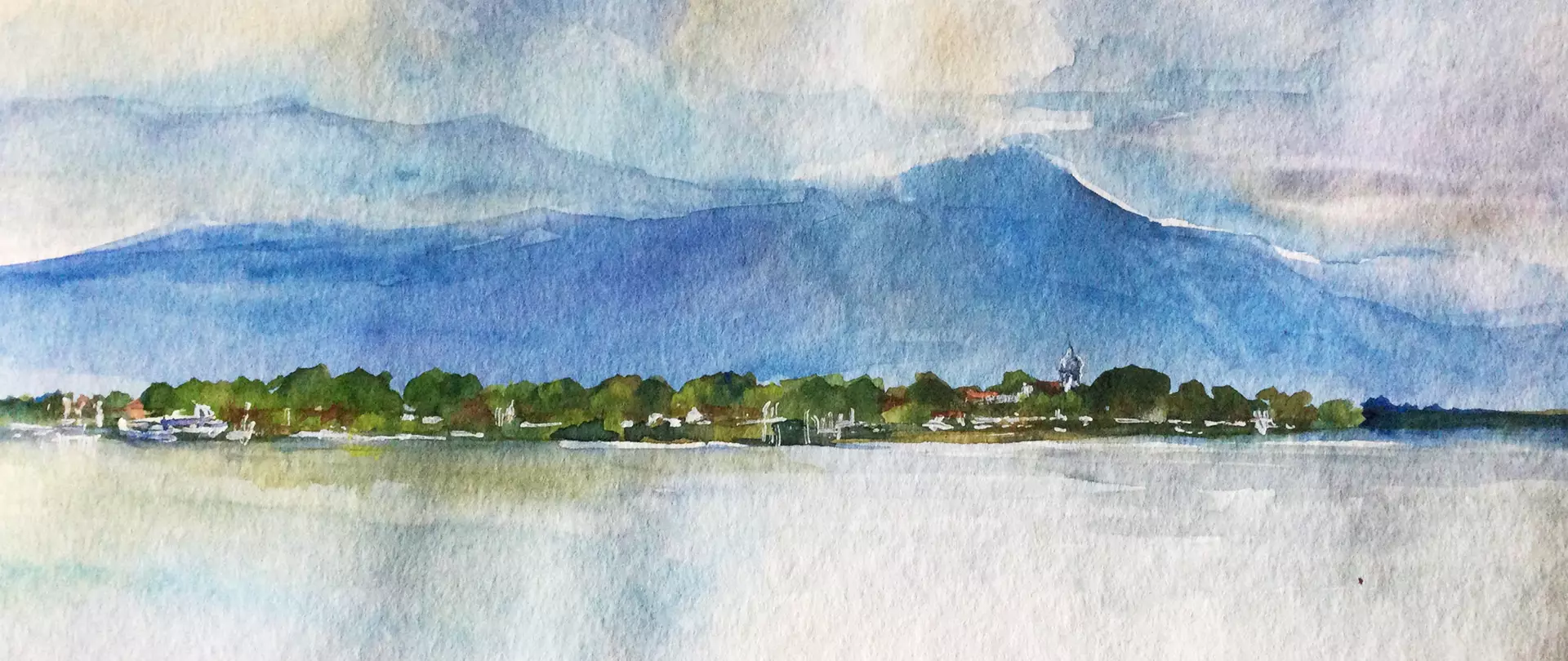 Aquarellmalerei einer Landschaft mit einem See im Vordergrund, einer Baumreihe und Gebäuden in der Mitte und einem großen blauen Berg im Hintergrund erstellt von artistravel Dozent Franz Schwarz