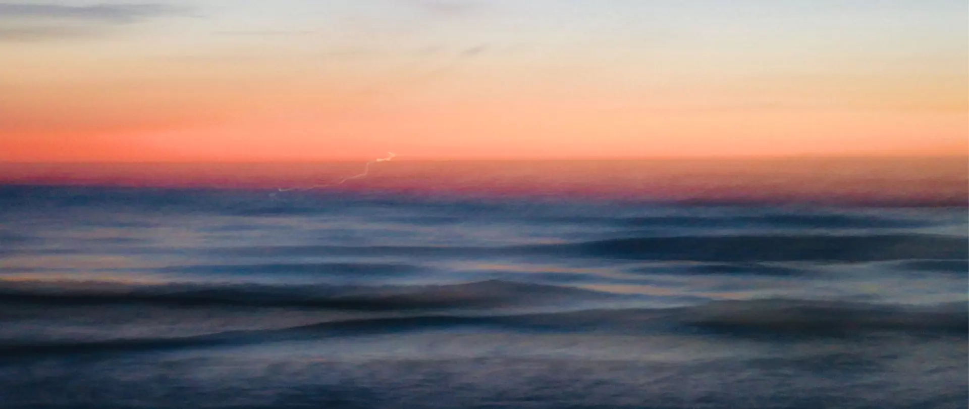 Weiches Meer mit sanften Wellen vor einem farbenfrohen Sonnenuntergang an der Küste von Amrum bei künstlerischer Naturfotografie