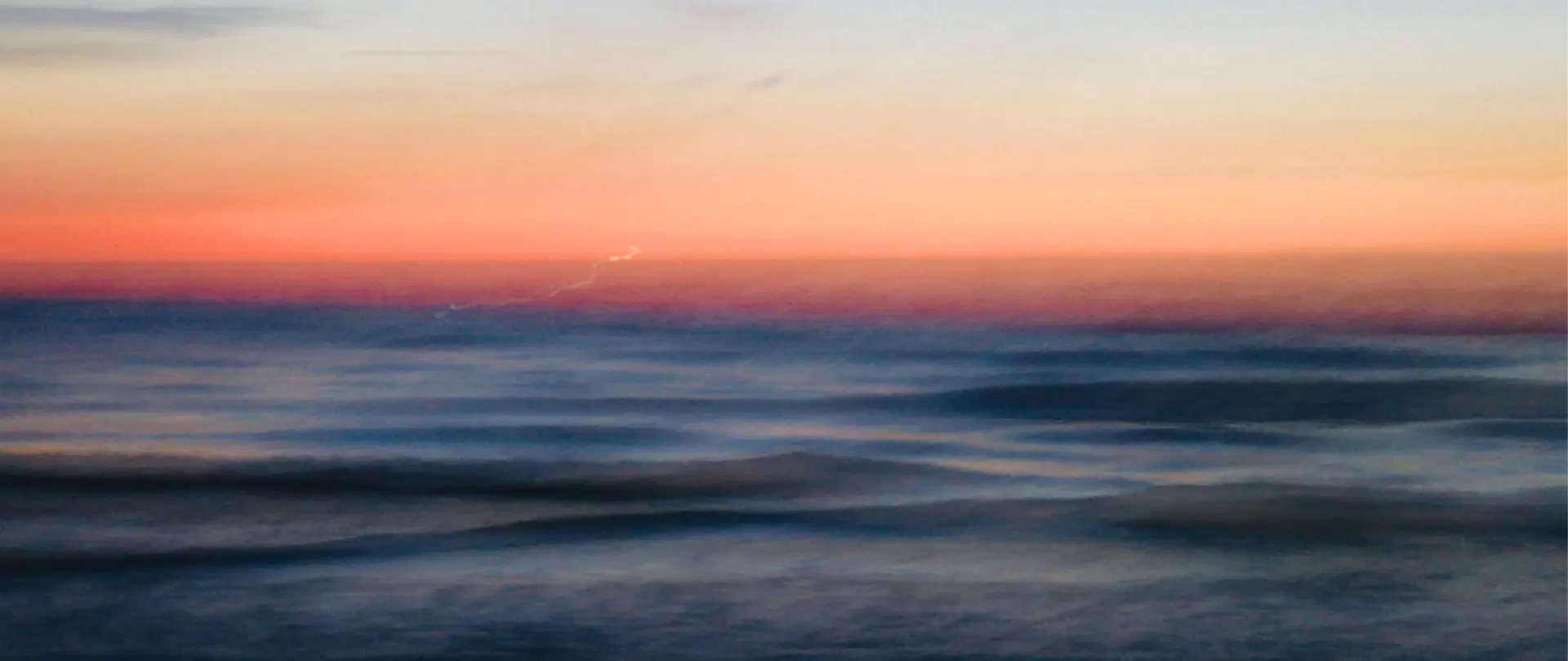 Weiches Meer mit sanften Wellen vor einem farbenfrohen Sonnenuntergang am Himmel, abstrakte künstlerische Landschaftsfotografie