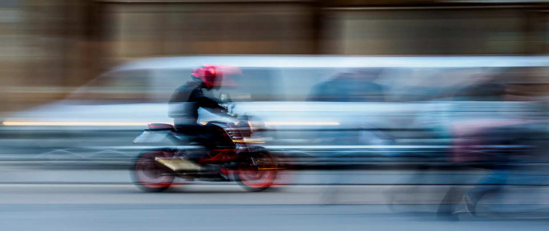 Motorradfahrer in rotem Helm und Bewegungseffekt vor verschwommenem Autoverkehr auf urbaner Straße für kreativen Fotoworkshop Bewegung