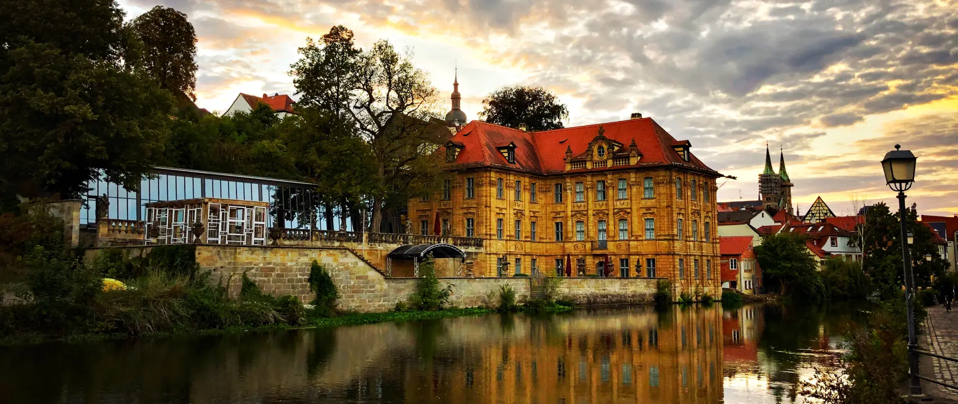 Historische Altstadt von Bamberg mit festlich geschmückten Straßen und Reflexion im Wasser bei Sonnenuntergang, ideale Kulisse für traditionelle Reportagefotografie