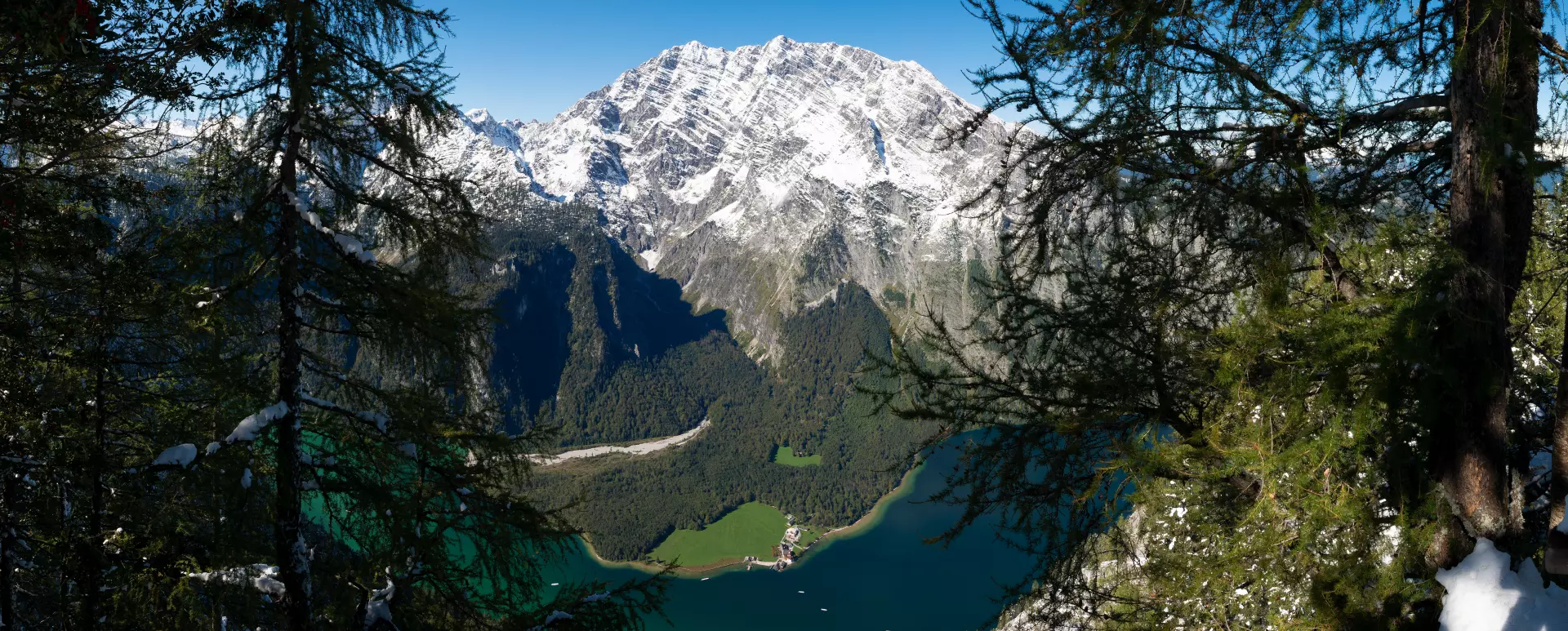 Panoramablick auf den Königssee und den Watzmann in Bayern mit verschneiten Berggipfeln und grünem Tal, eingerahmt von Bäumen