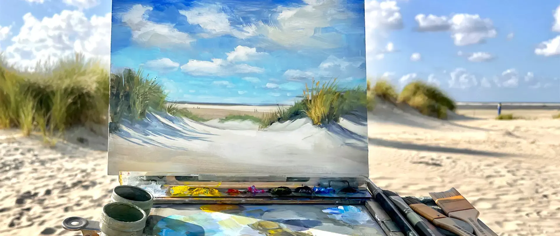 Plein Air Spiekeroog Malkurs am Strand mit Staffelei, Gemälde der Dünenlandschaft und Pinsel vor dem natürlichen Dünenhintergrund unter blauem Himmel