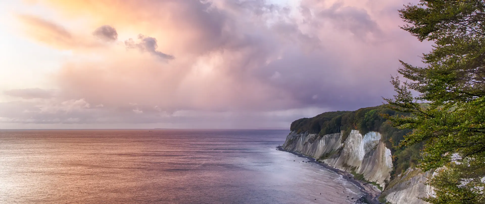 Küstenlandschaft auf Rügen mit steilen Kreidefelsen, ruhigem Meer und dramatischem Himmel im warmen Licht der Abenddämmerung