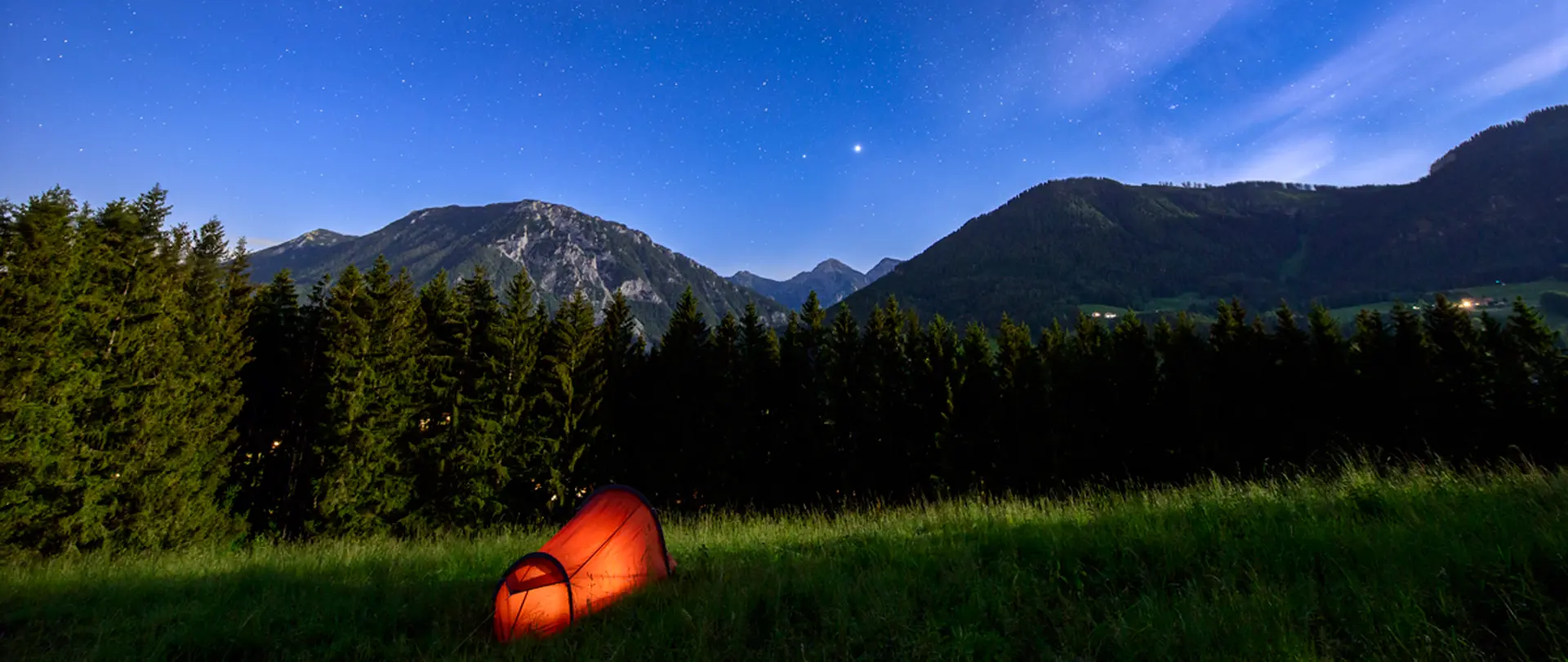 Rotes Zelt auf einer Wiese vor Alpenbergen bei Sternenhimmel als Motiv für kreative Naturfotografie und persönliche Bildsprache