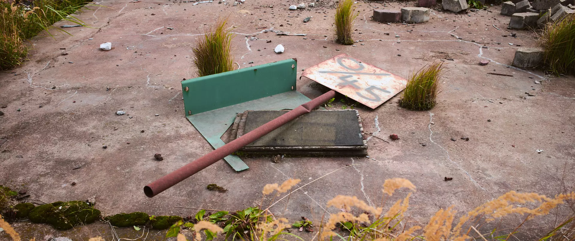 Umgestürztes, verrostetes Verkehrsschild liegt auf einem verwitterten Boden mit Gras und geschichtsträchtiger Atmosphäre