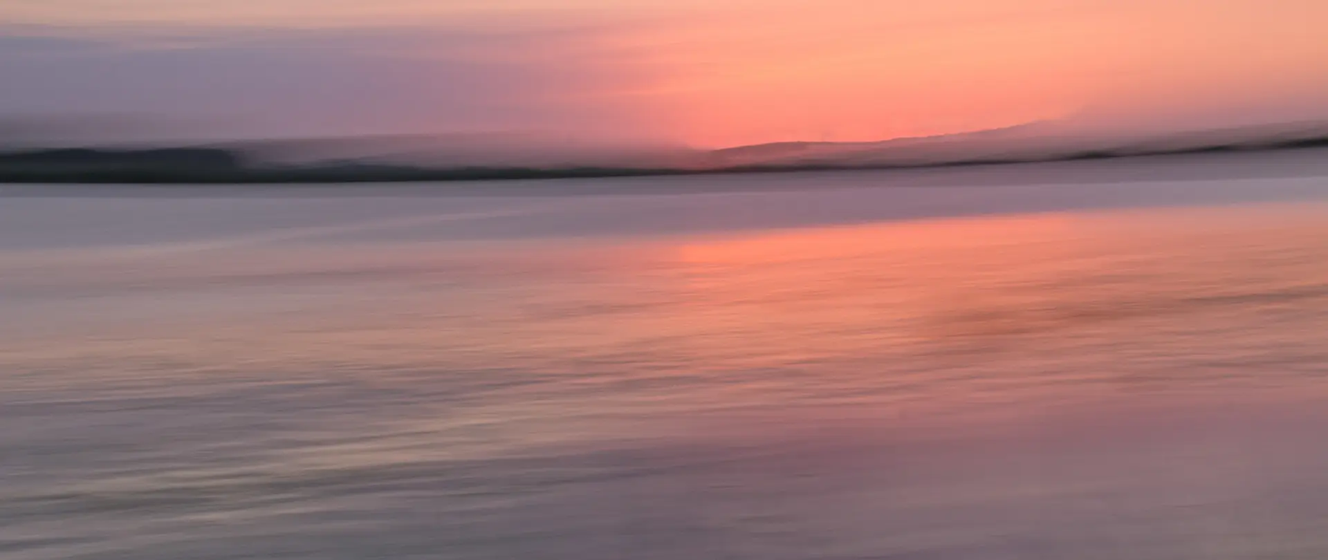 Sanfte Lichtreflexionen bei Sonnenuntergang über ruhigem Gewässer mit unscharfer Insel im Hintergrund, inspiriert vom Fotokurs Insellicht