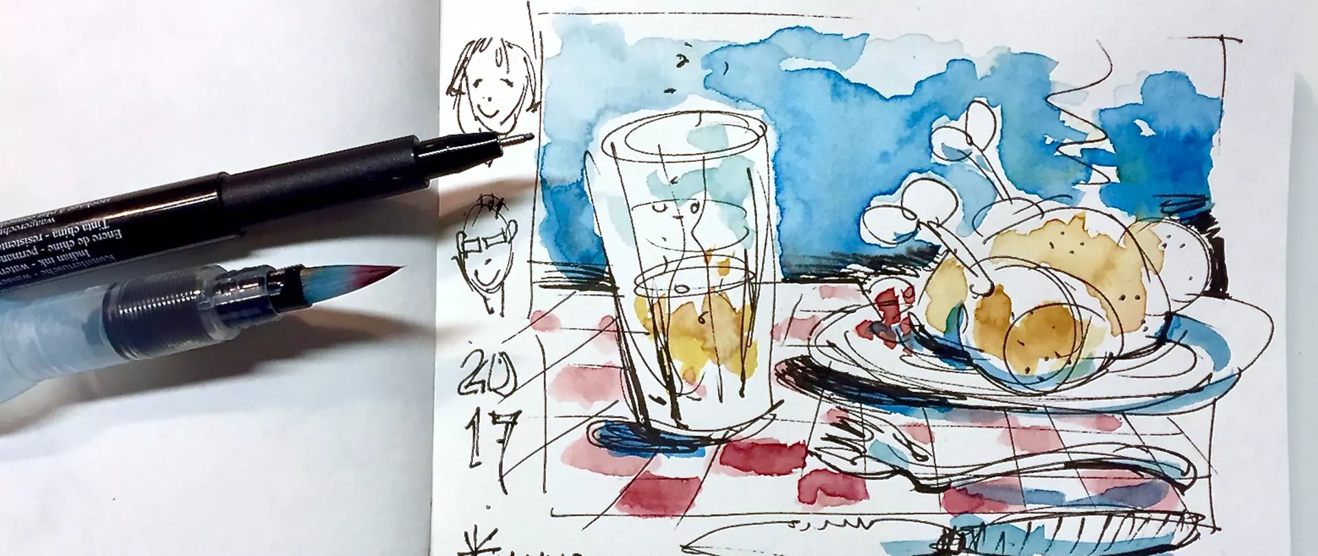 Skizze eines gedeckten Tisches mit einem Glas und einem Teller mit Hähnchenschenkeln, daneben zwei Zeichenstifte auf einem Skizzenbuch