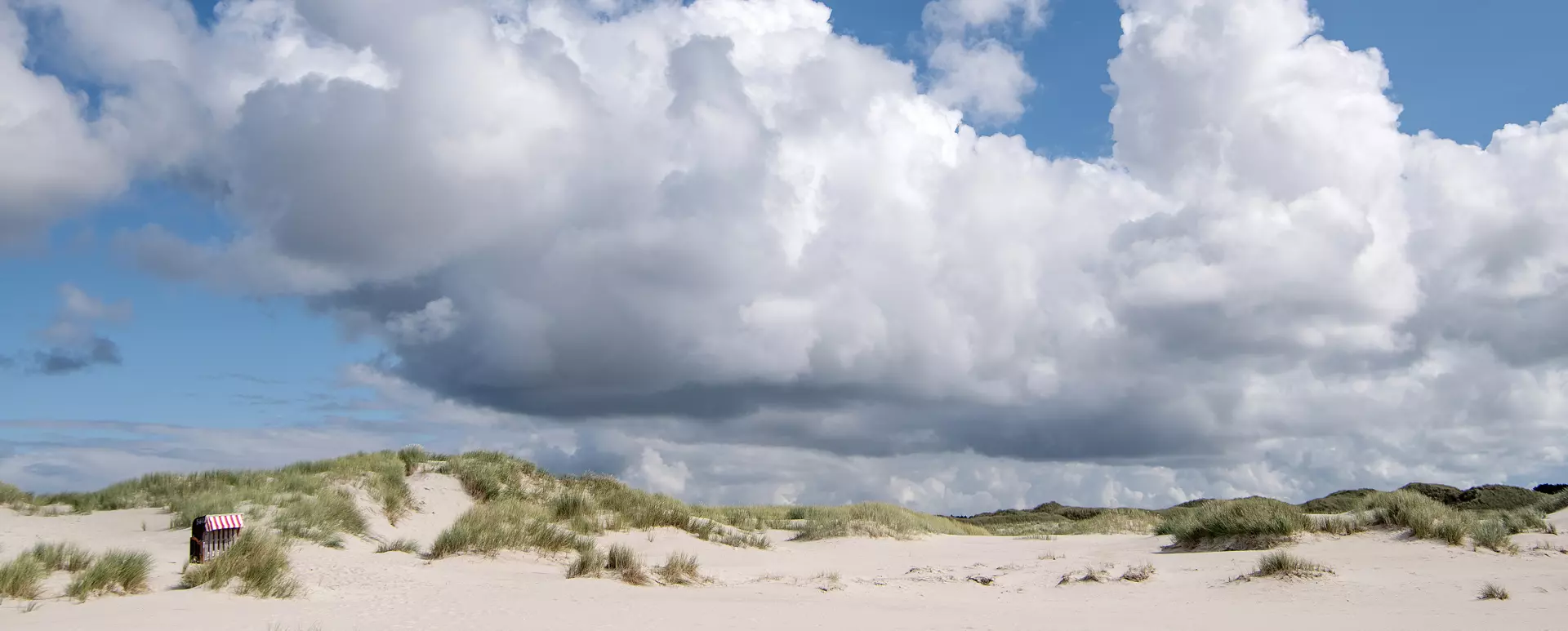 Weite Dünenlandschaft mit Strandkorb und markante  Wolken bei Sommerstimmung