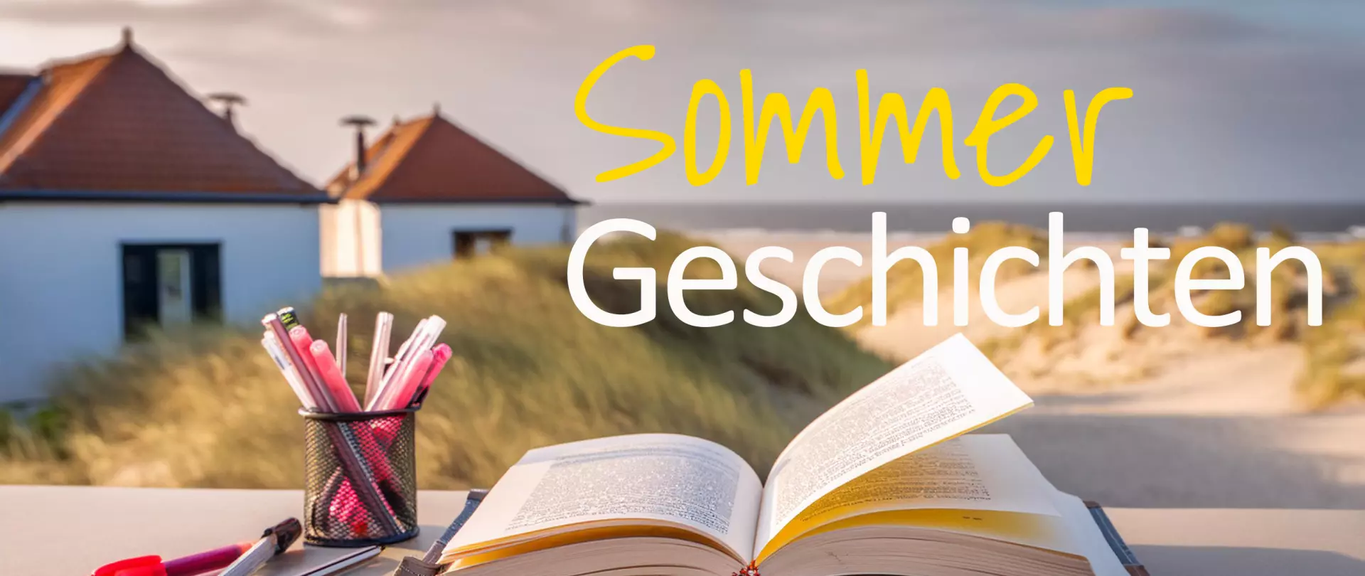 Offenes Buch und Stiftehalter mit Stiften auf einem Tisch vor Dünen und Häusern, Text 'Sommer Geschichten'