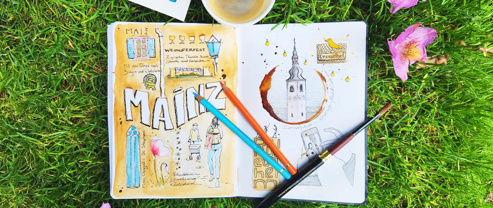 Skizzenbuch mit Aquarellen, Kaffeeflecken, Stiften und Pinsel auf Gras, Thema Mainz und Reiseillustrationen, um kreatives Malen mit Kaffee zu zeigen