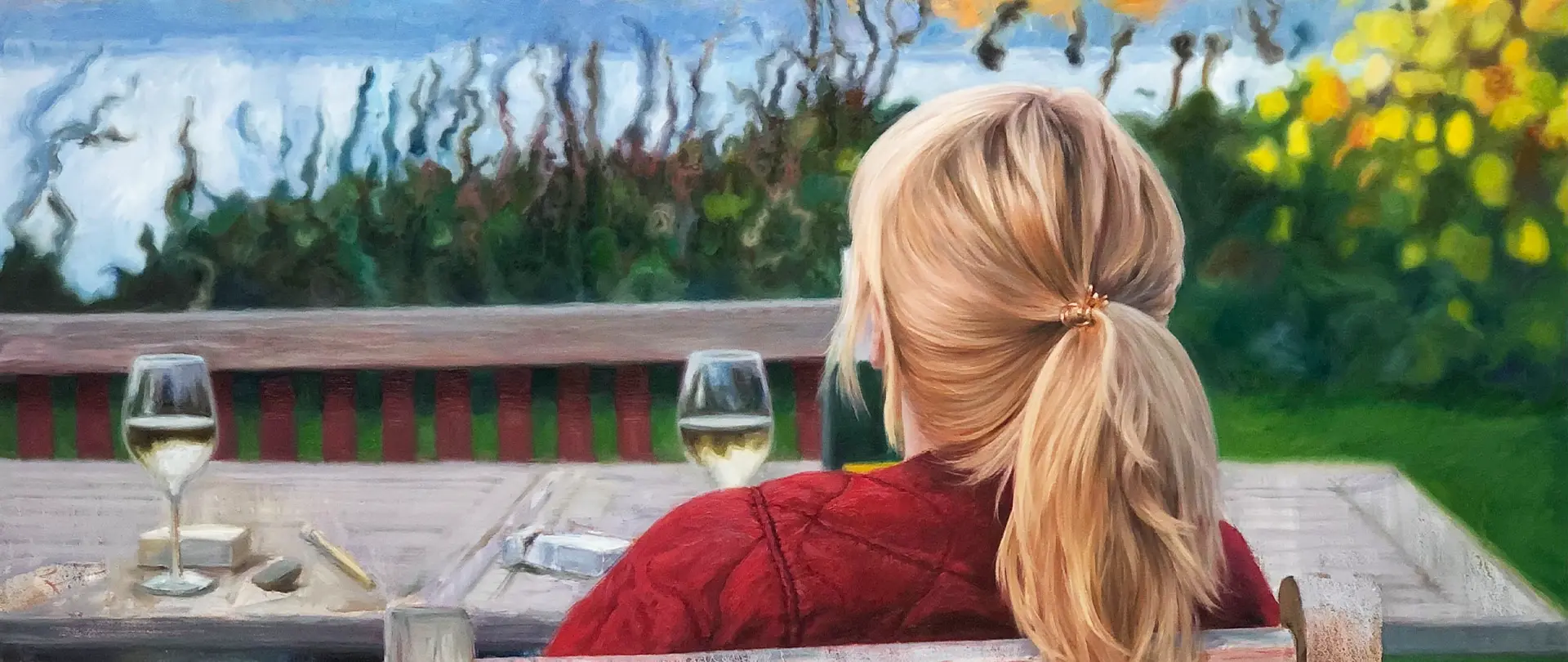 Portrait und Figur Frau mit blondem Pferdeschwanz in rotem Pullover sitzt draußen an einem Tisch mit zwei Weingläsern in malerischer Gartenlandschaft