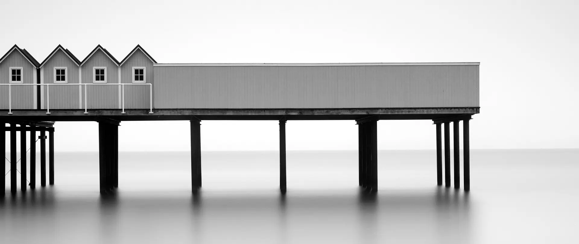 Fine Art Photography - Basics Minimalistische Schwarz-Weiß-Aufnahme eines Pier mit kleinen Häusern über ruhigem Wasser für Fine Art Photography Grundlagen