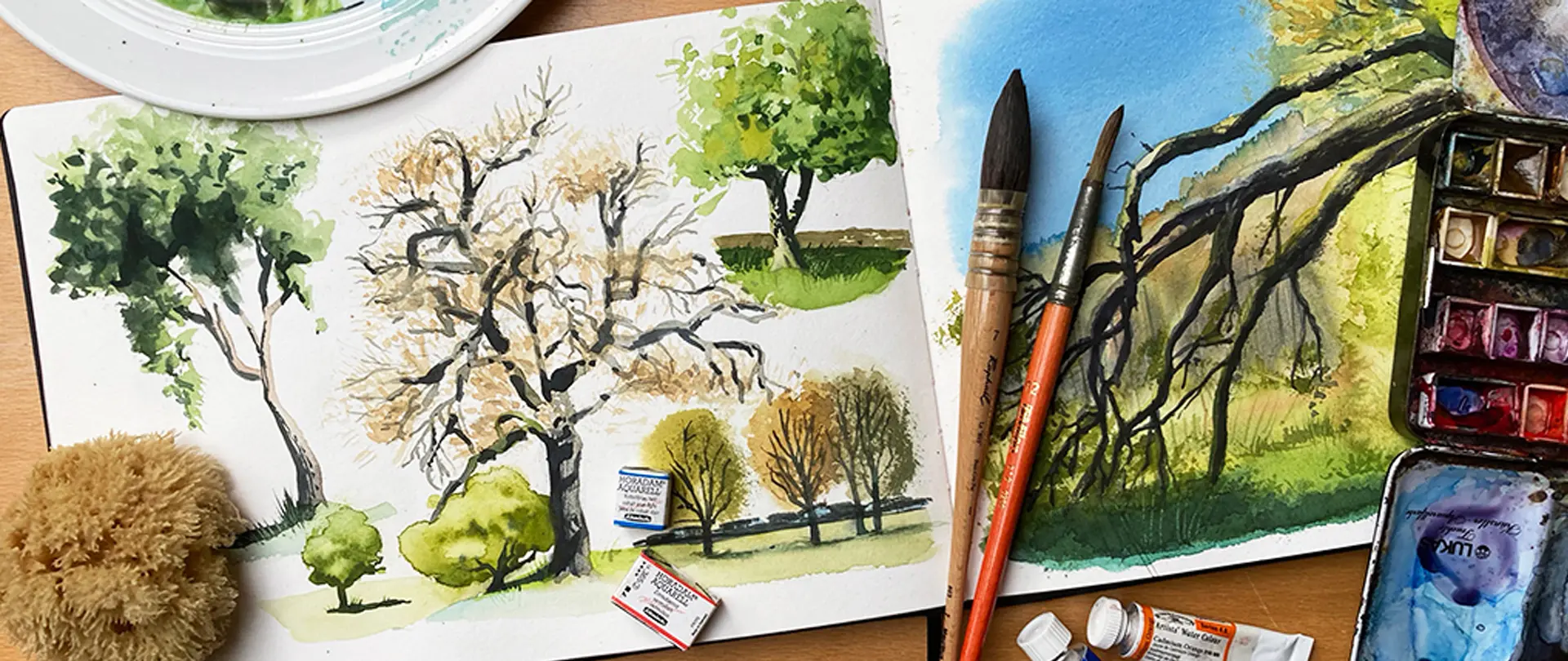 Aquarellskizzen verschiedener Bäume und Pinsel auf einem Arbeitstisch, die natürliche und lockere Darstellungen von Baumformen zeigen