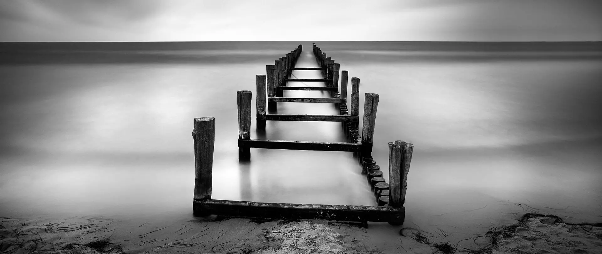 Langzeitbelichtung einer verlassenen Holzpier an der ruhigen Ostsee im Herbst mit sanftem Nebel und minimalistischer Schwarz-Weiß-Ästhetik