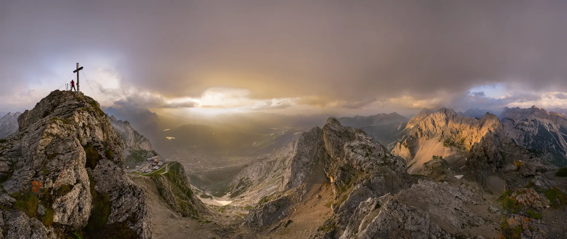 Panoramablick auf die Karwendelregion mit Felsen, Berggipfeln, Kreuz und dramatischem Licht für kreative Reisefotografieübungen