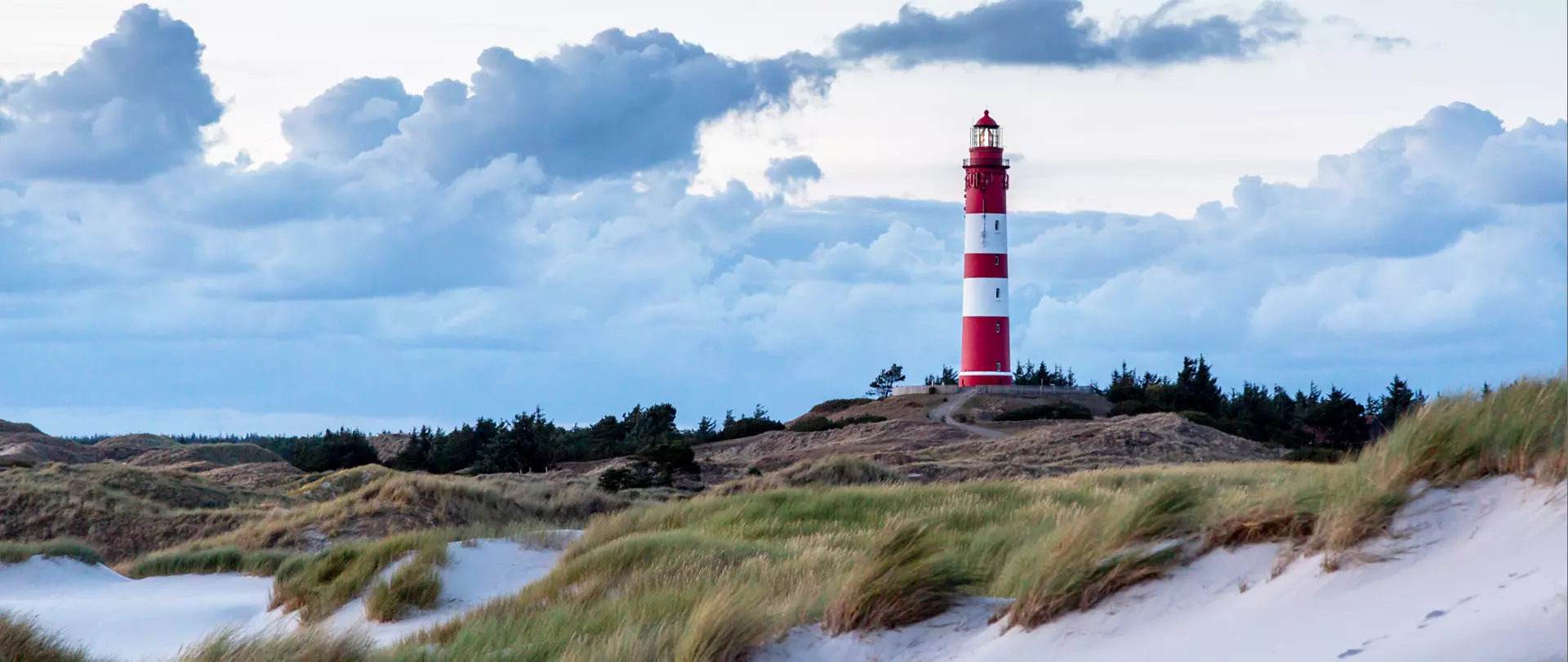 Leuchtturm mit rot-weißen Streifen in Dünenlandschaft bei bewölktem Himmel für Fotografie mit natürlichem Licht