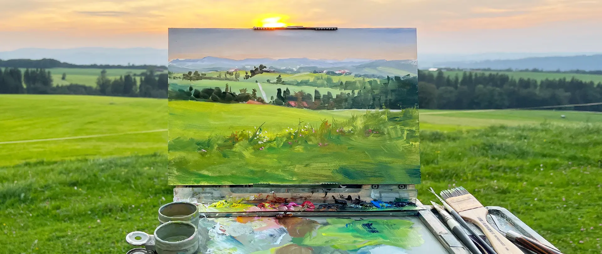 Landschaftsmalerei in Öl - Pleinair Ölgemälde einer grünen Landschaft im Freien mit Malutensilien und Pinsel vor Sonnenuntergang auf Wiese, Impression einer Pleinair-Landschaftsmalerei