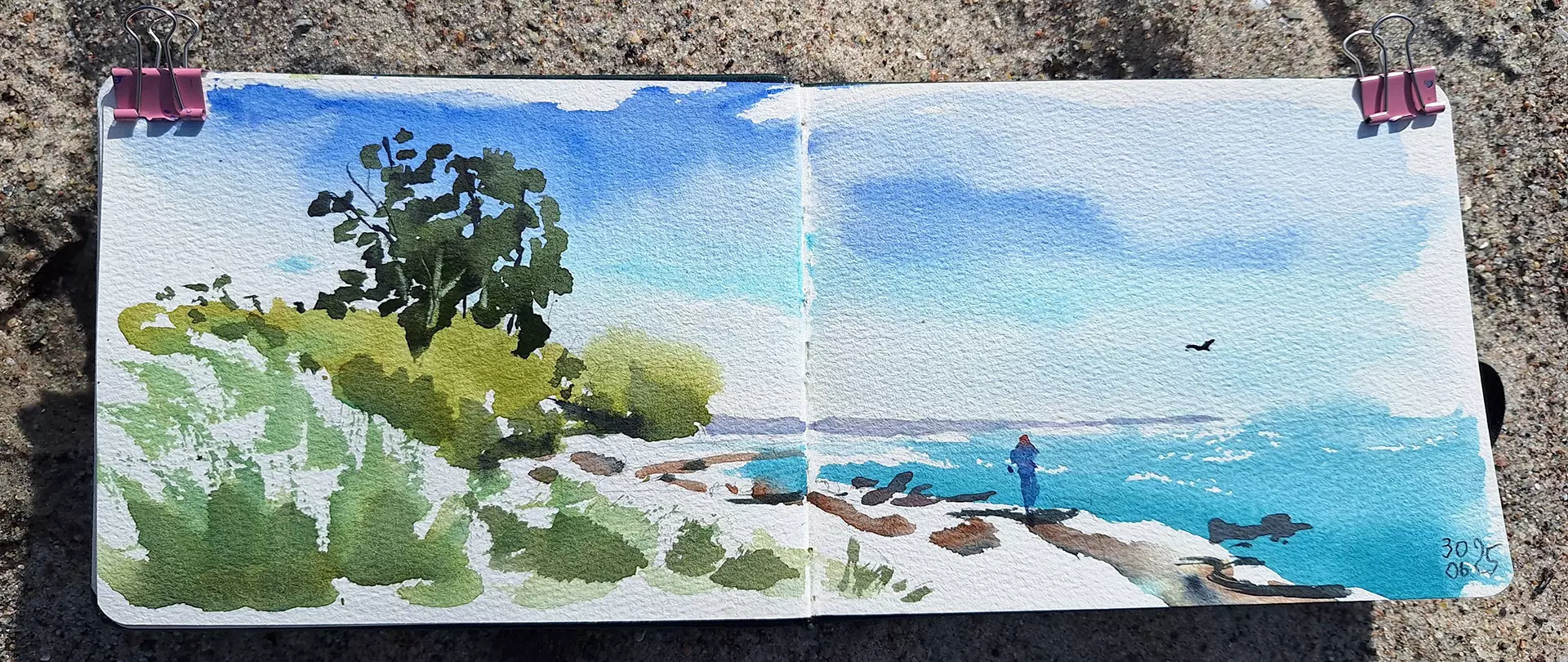 Stimmungsvolles Landschaftsaquarell eines Küstenabschnitts mit Bäumen, Meer, Steinen und einer Person, entstanden im Skizzenbuch direkt vor Ort