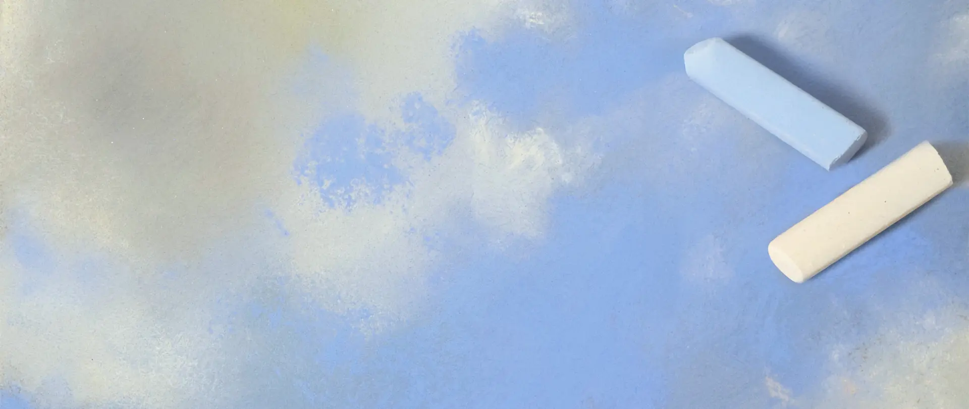 Zwei Pastellkreiden auf blauem Untergrund mit weißen Farbsprenkel, die eine Wolkenstudie in Pastell darstellen