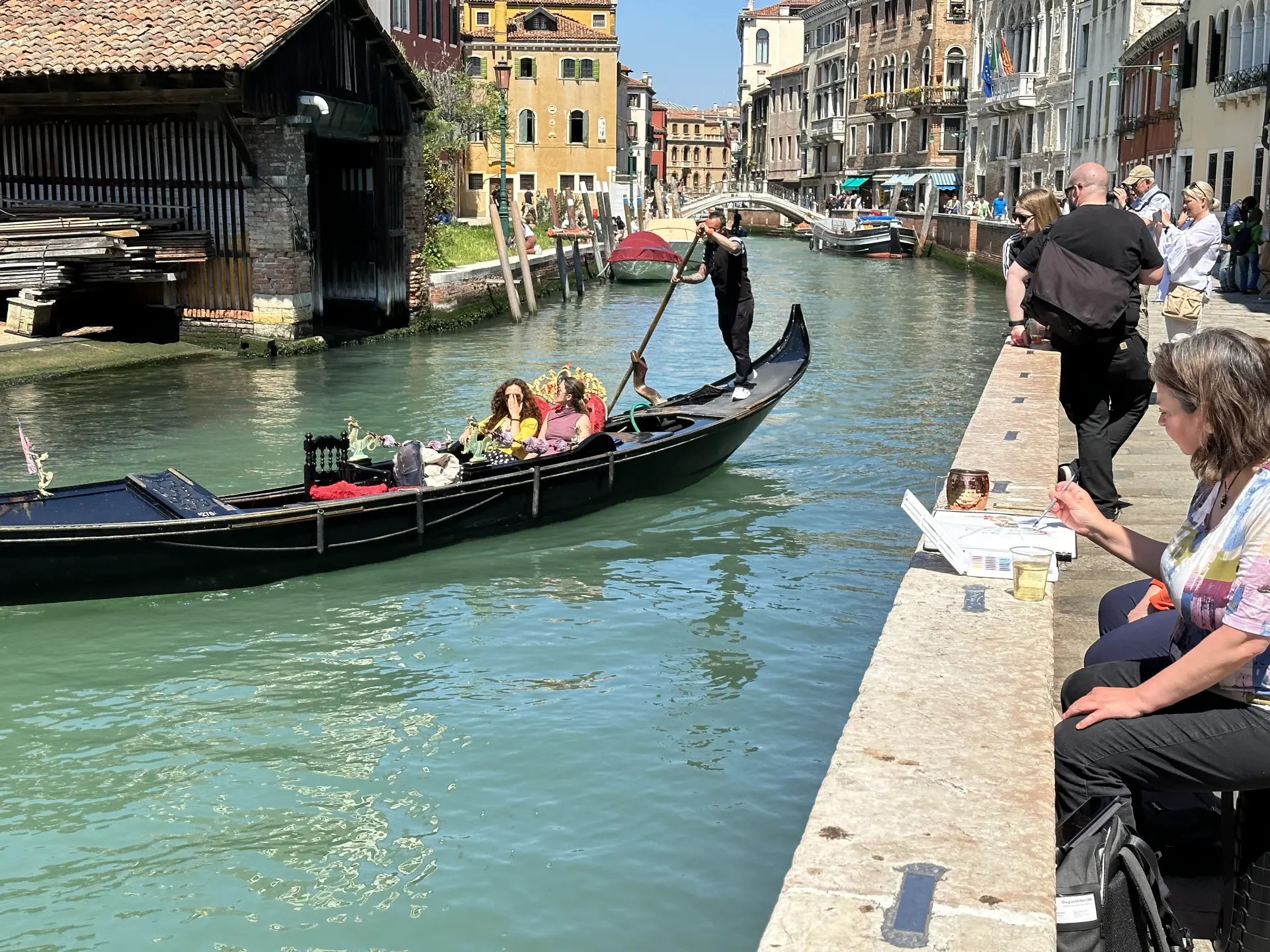 Gondel trifft Skizzenbuch Gondelfahrt in Venedig mit Touristen und Skizzenbuchzeichner, der am Ufer des Kanals sitzt und zeichnet