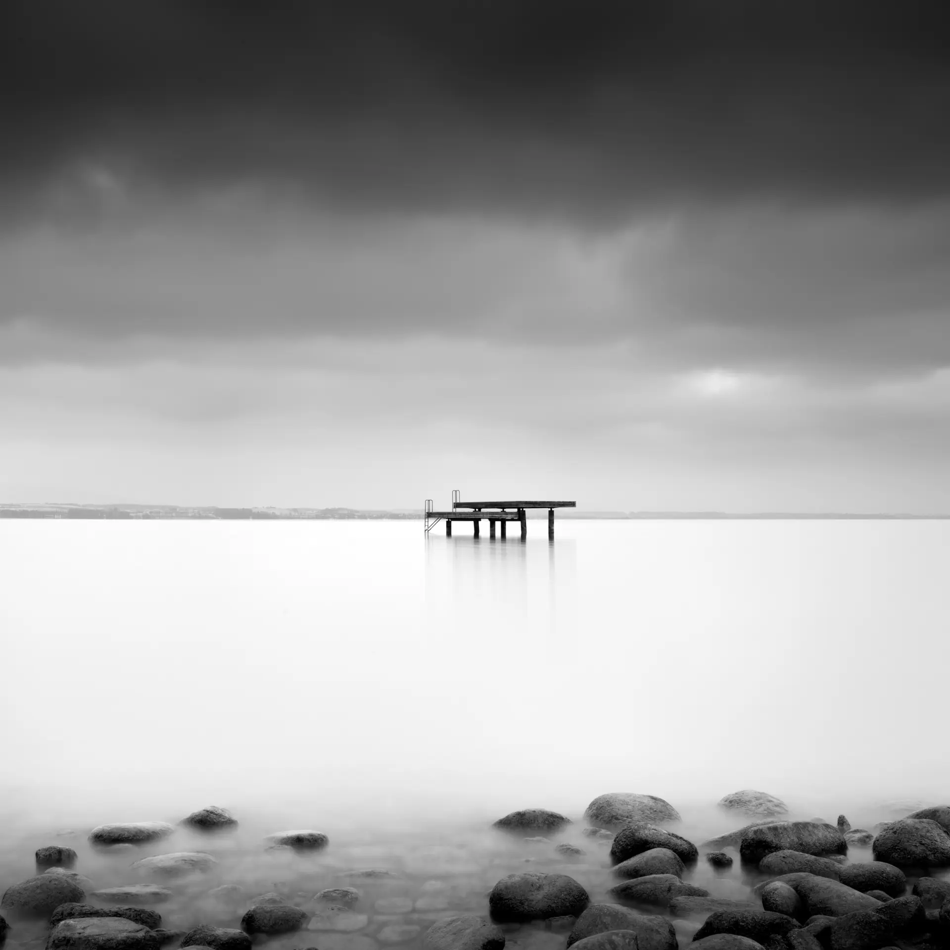 Steg auf ruhigem Bodensee-Wasser mit steiniger Uferlinie und dramatischem Himmel für reduzierte Fine Art Fotografie am westlichen Bodensee
