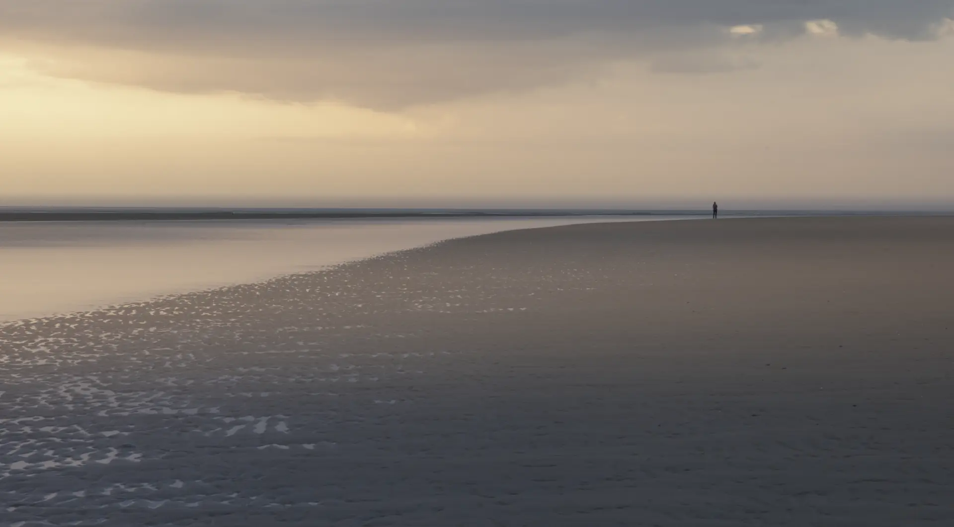 Weite Nordseestrandlandschaft auf Spiekeroog bei ruhiger Stimmung mit Einzelperson am Horizont und sanftem Licht vor Sonnenuntergang