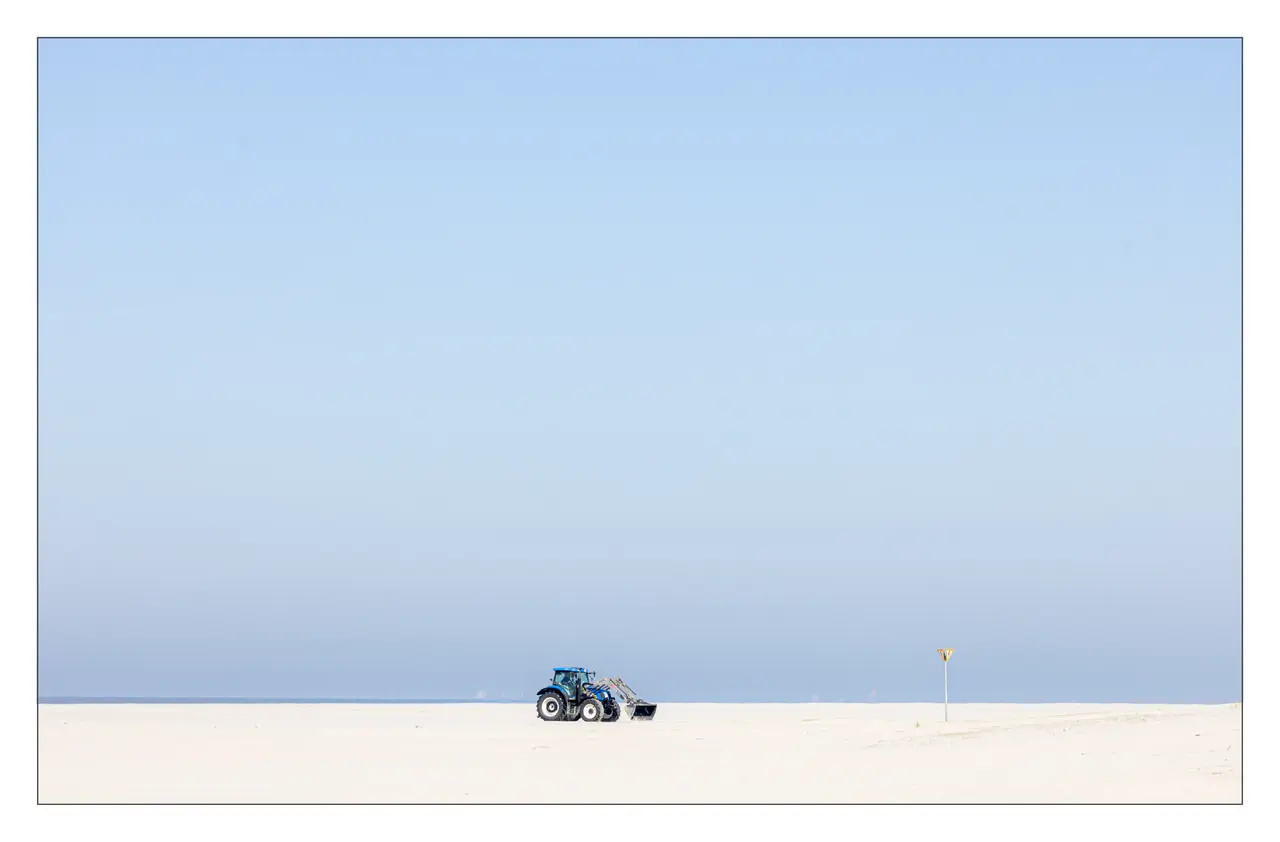Blauer Traktor auf leerem Strand bei klarem Himmel auf der ruhigen Nordseeinsel Spiekeroog außerhalb der Hochsaison