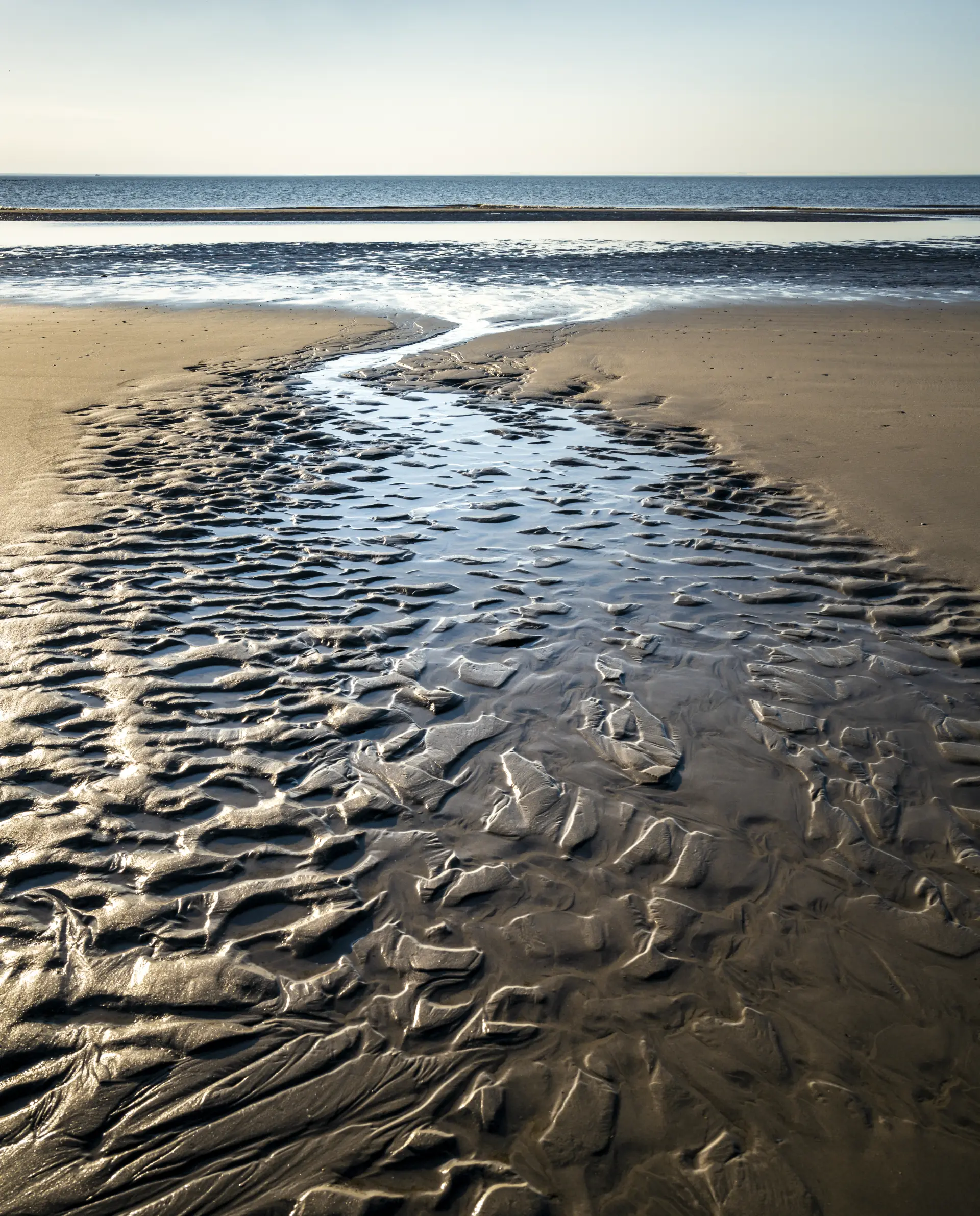 Spiegelndes Wasserlaufbett im Watt mit weiter Nordseeküste bei ruhigem Licht auf Spiekeroog, ideal für Landschafts- und Naturfotografie in Abgeschiedenheit