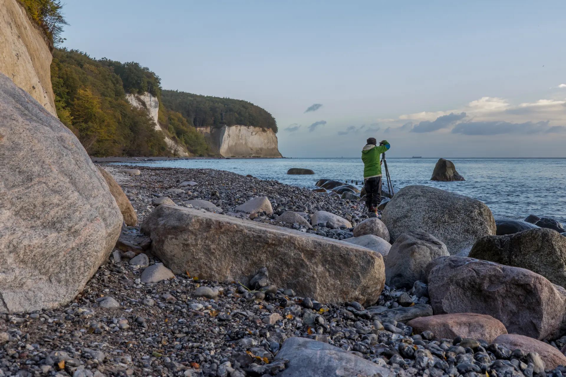 Fotograf am felsigen Strand der Insel Rügen mit Kreidefelsen im Hintergrund bei ruhigem Meer und klarem Himmel zur kreativen Landschaftsfotografie