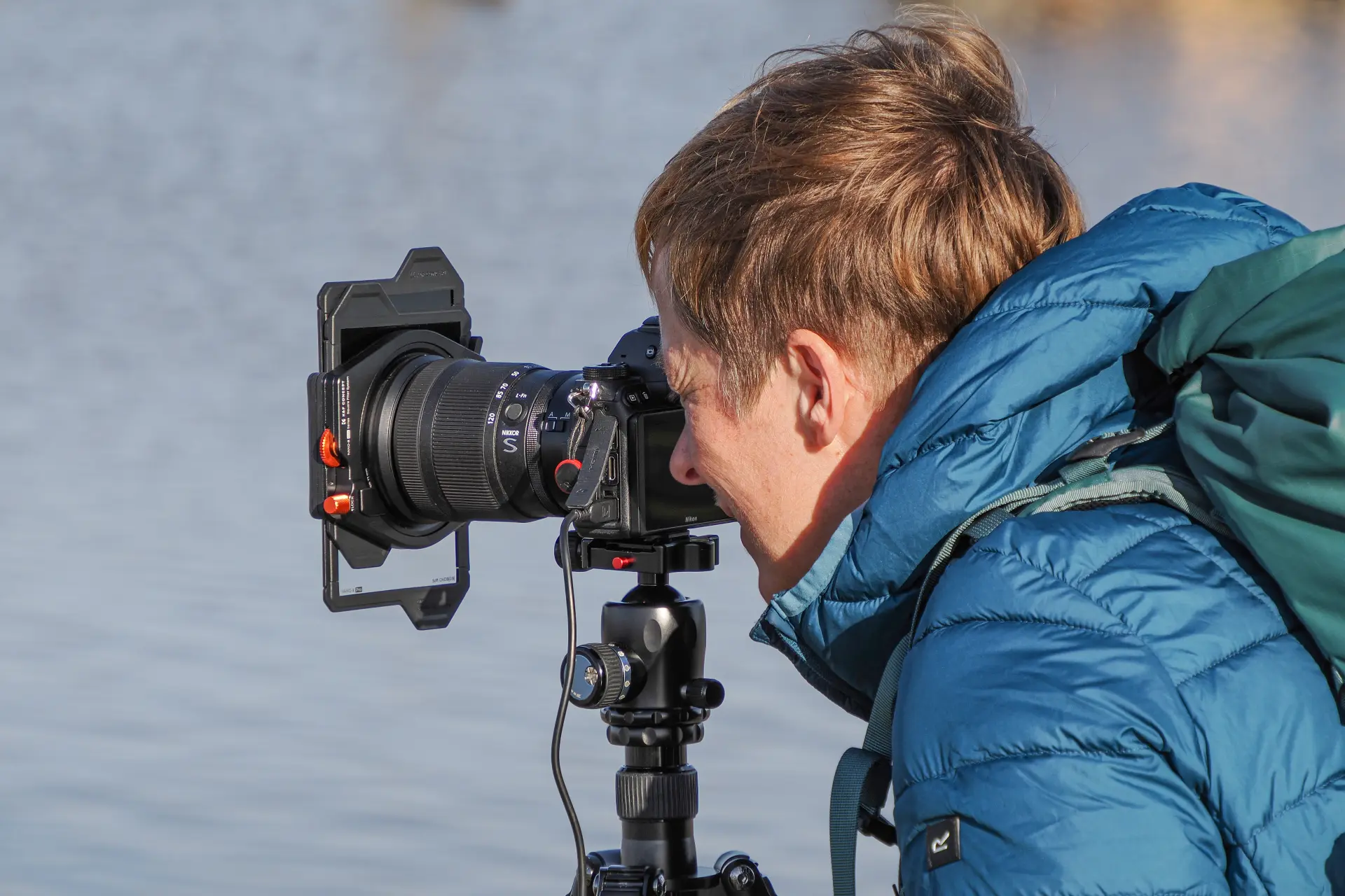 Person in blauer Jacke fotografiert mit Kamera auf Stativ Langzeitbelichtung von Wasser bei weichem Licht und surrealer Stimmung am Meer