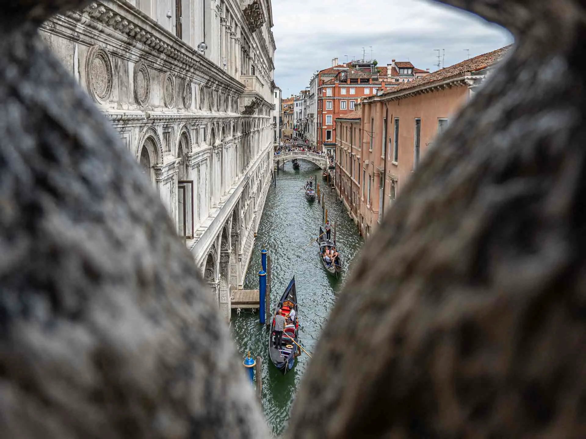 Blick durch eine Öffnung auf einen venezianischen Kanal mit mehreren Gondeln, die Bewegung und Dynamik in der Stadtfotografie zeigen