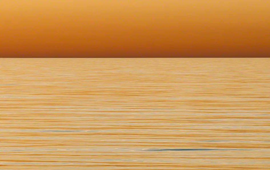 Sonnenuntergang über der ruhigen Nordsee mit orangefarbenem Himmel und sanftem Wasser vor der Dünenlandschaft der Insel Amrum