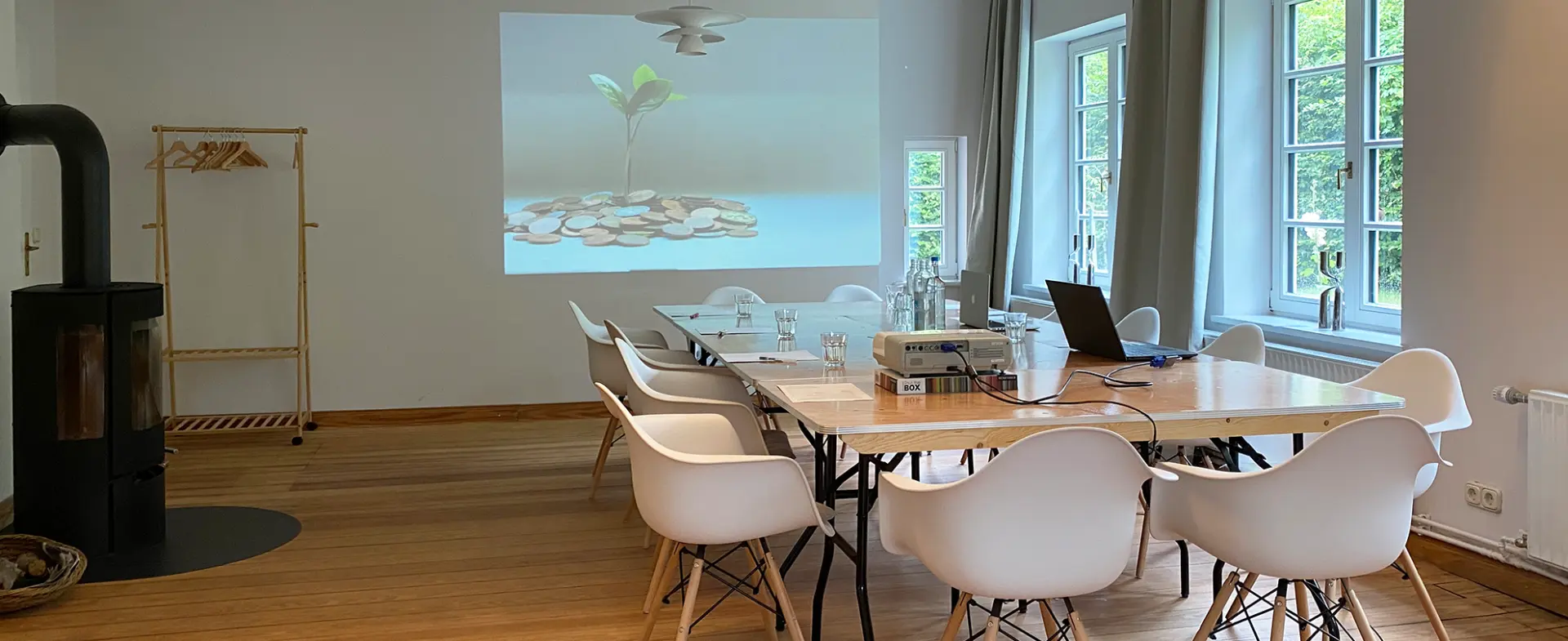 Konferenzraum mit Holztisch, weißen Stühlen, Laptop und Beamer im Naturpark Aukrug