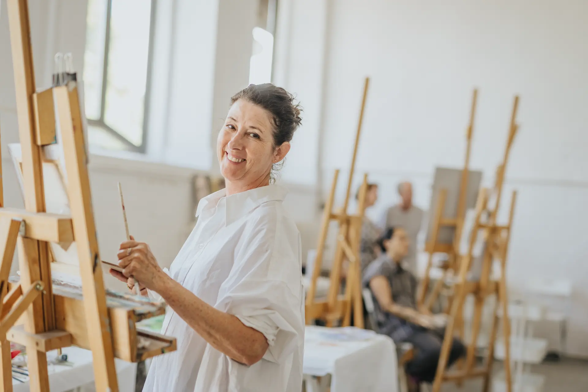 Atelier Alte Molkerei in Hattingen Frau in Worpswede malt an Staffelei in einem hellen Atelier mit weiteren Personen und Staffeleien im Hintergrund