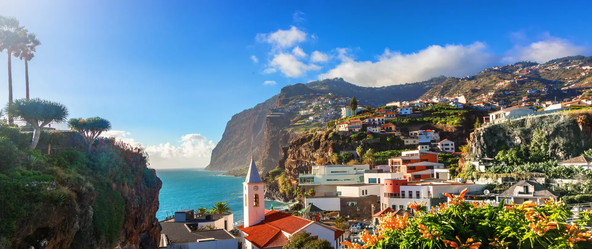 Küste mit bunten Häusern, steilen Klippen und blauem Atlantik unter strahlendem Himmel in Portugal