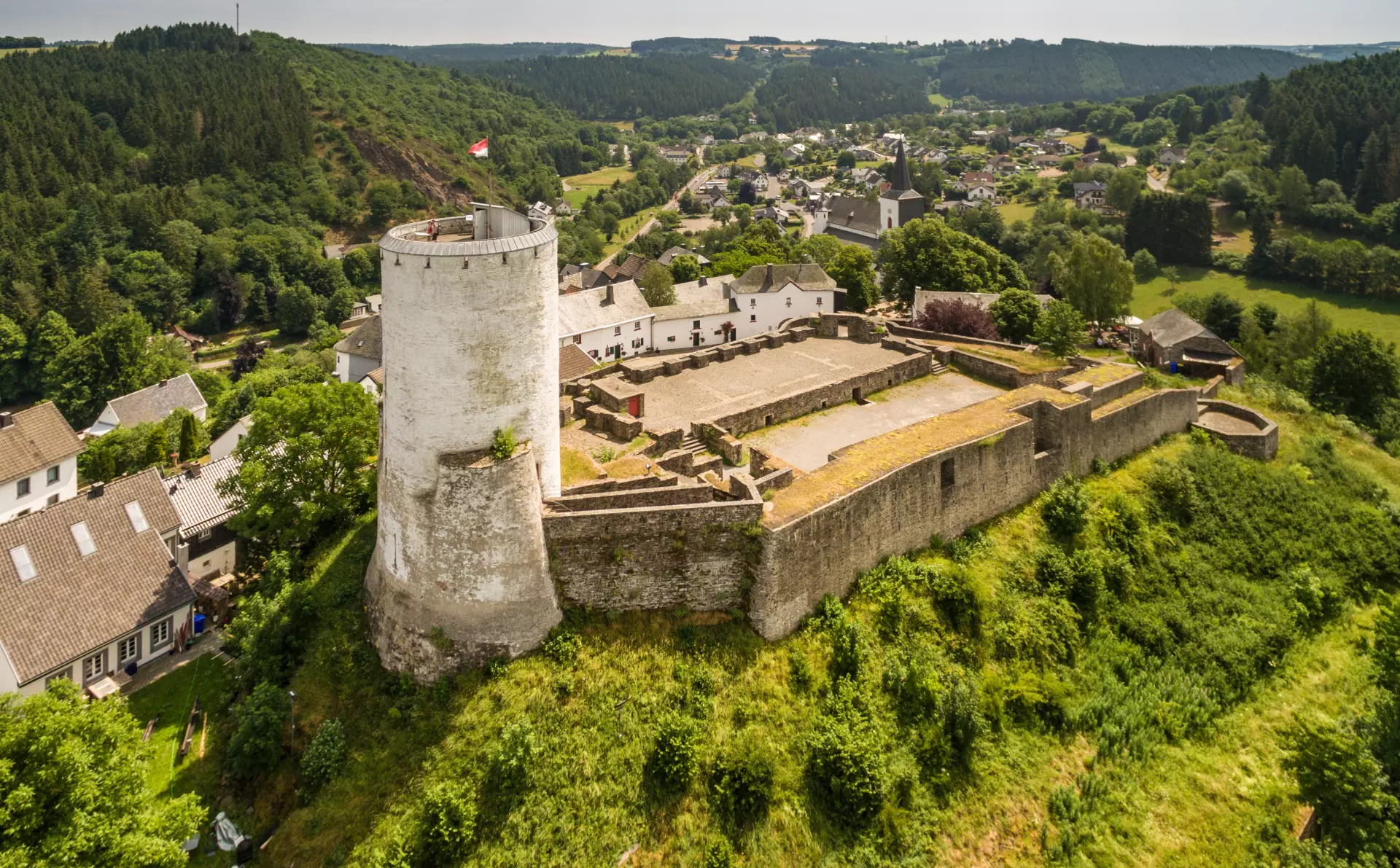Burg Reifferscheid Burg mit rundem Wehrturm in der Eifel umgeben von grünen Hügeln und einem Dorf im Hintergrund unter klarem Himmel