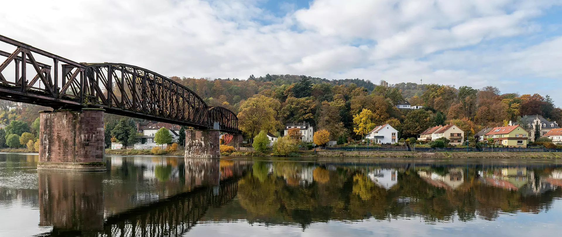 Eisenbahnbrücke über ruhigen Fluss mit herbstlich bunten Bäumen und Häusern in Hameln-Pyrmont
