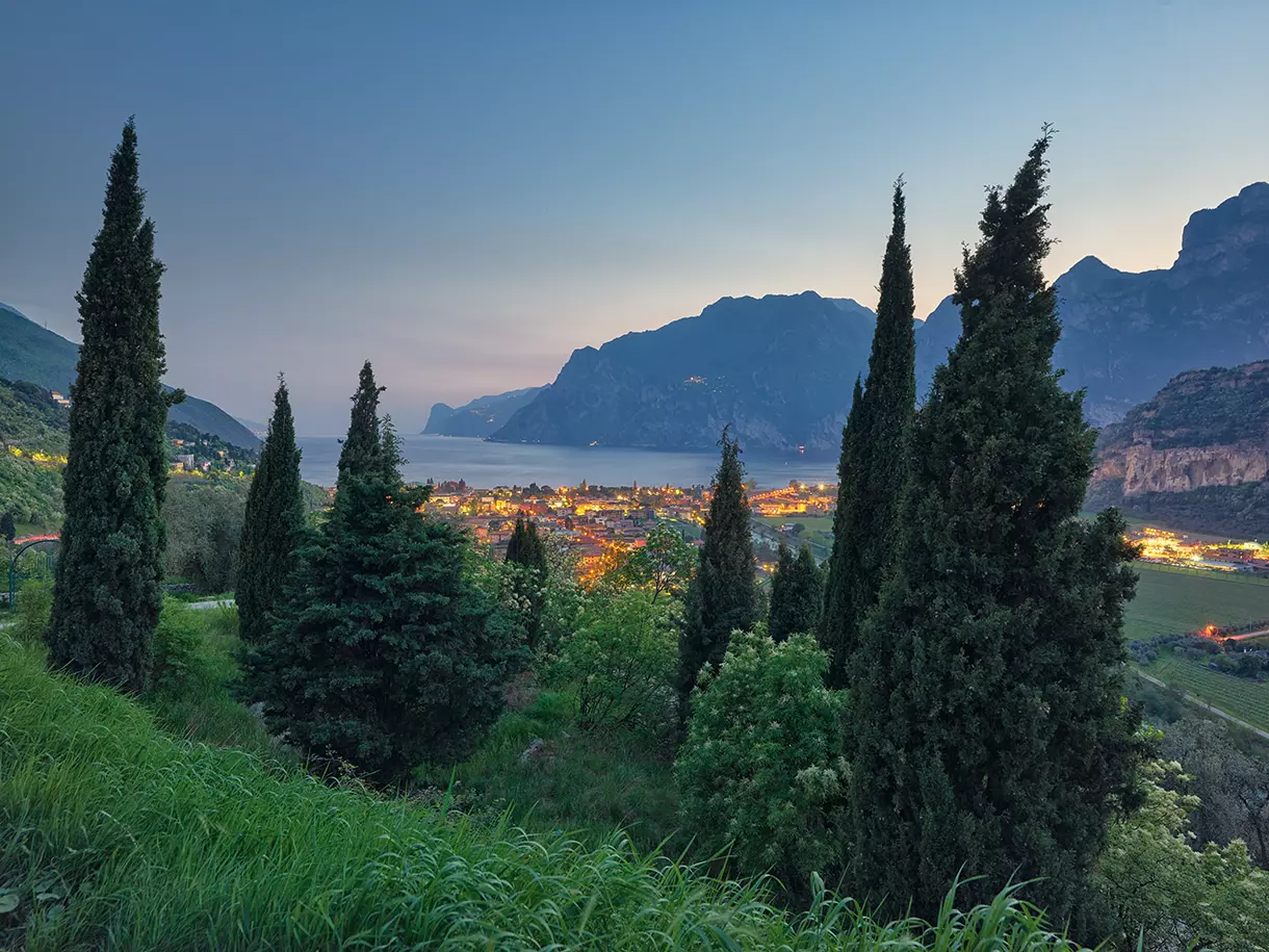 Außenstehender Blick auf den Gardasee Außenstehender Blick auf den Gardasee mit einem Wald im Vordergrund, die Stadtregion dahinter sowie Blick auf das Meer und die Berge