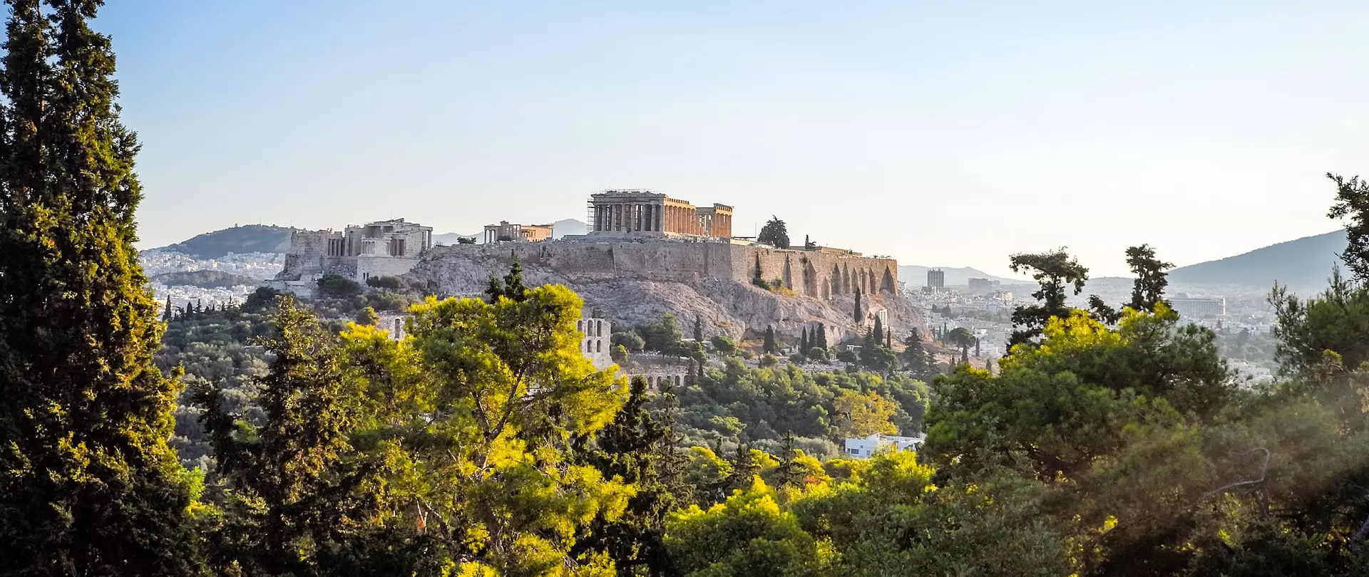 Akropolis von Athen mit dem Parthenon-Tempel auf einem Hügel, umgeben von grünem Wald und urbaner Landschaft im Hintergrund