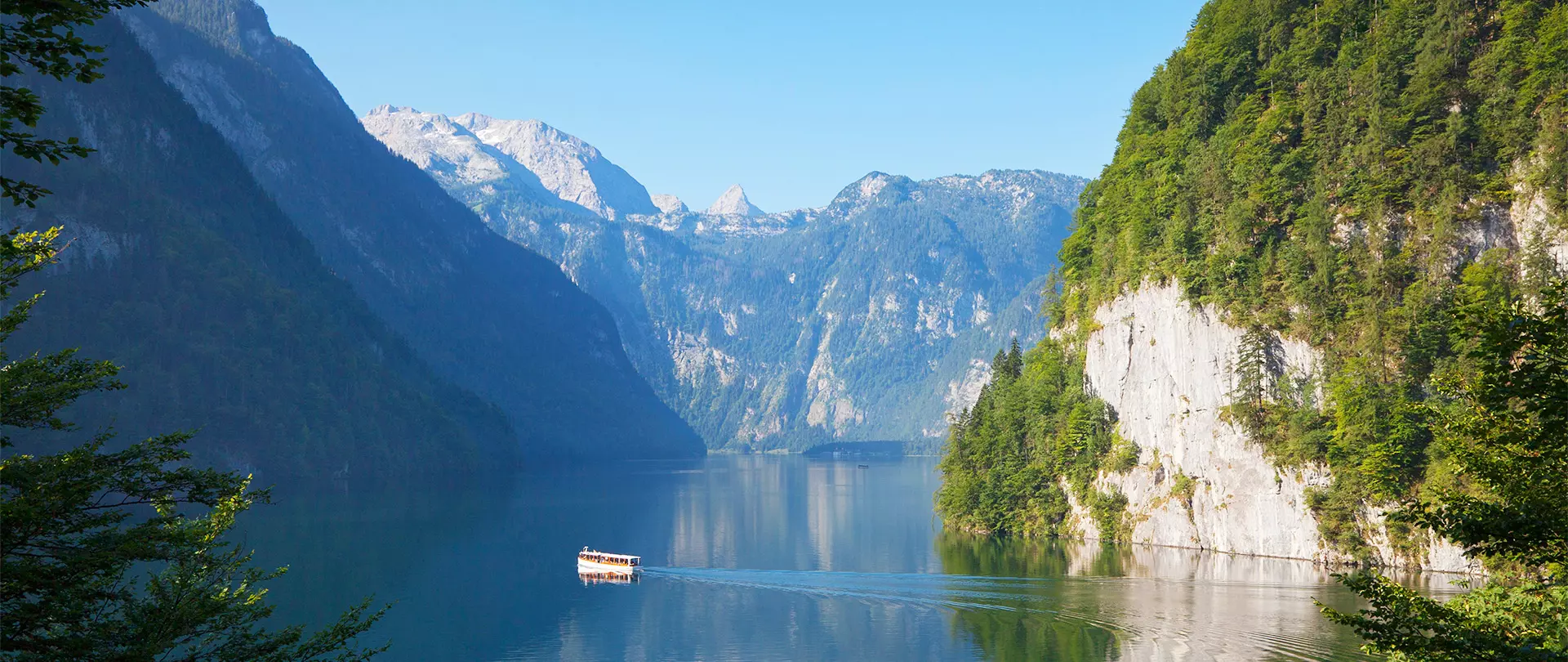 Klares Bergpanorama mit Königssee, steilen Felswänden und einem kleinen Boot auf ruhigem Wasser im Berchtesgadener Land