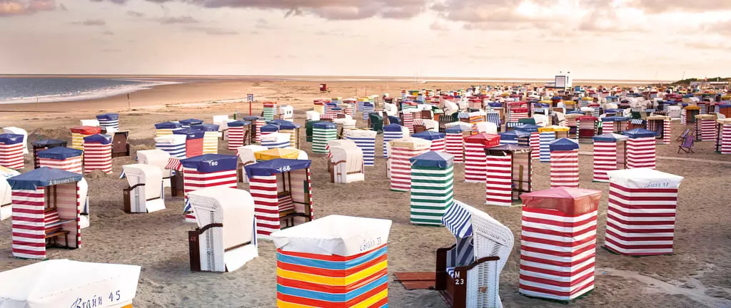 Strand in Borkum mit zahlreichen bunten Strandkörben in rot, blau, grün und weißen Streifen unter bewölktem Himmel