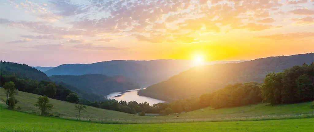 Sonnenuntergang über grünen Hügeln und einem Fluss in der malerischen Landschaft der Eifel