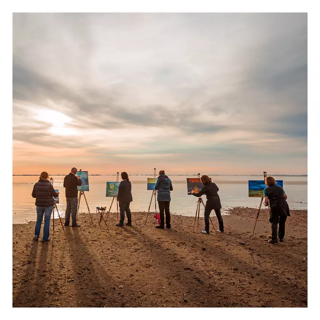 Sechs Personen malen mit Staffeleien am Strand von Föhr bei Sonnenuntergang, mit Blick auf das Meer und den wolkigen Himmel
