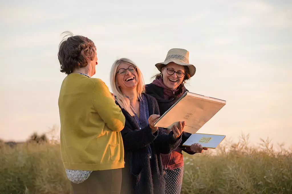 Drei Frauen lachen gemeinsam beim Betrachten von Dokumenten im Freien in der Moselregion bei Sonnenuntergang